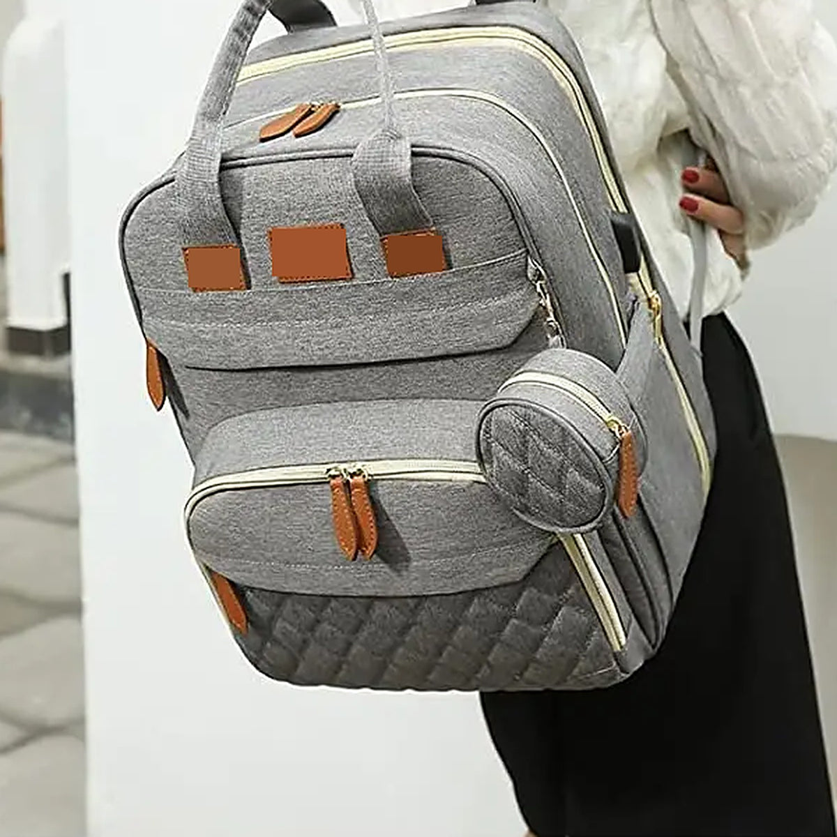 Gray diaper backpack worn on the back with its pacifier pouch clipped on the side